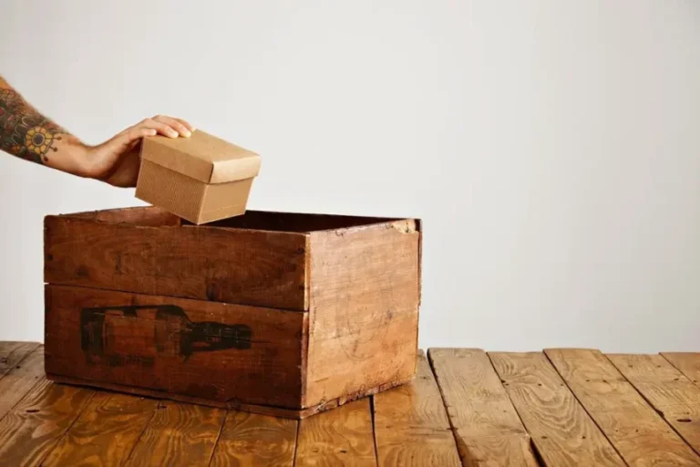 tattooed-hand-puts-blank-cardboard-package-with-gift-inside-ld-wooden-crate-rustic-table-isolated-white_346278-1632-860x573